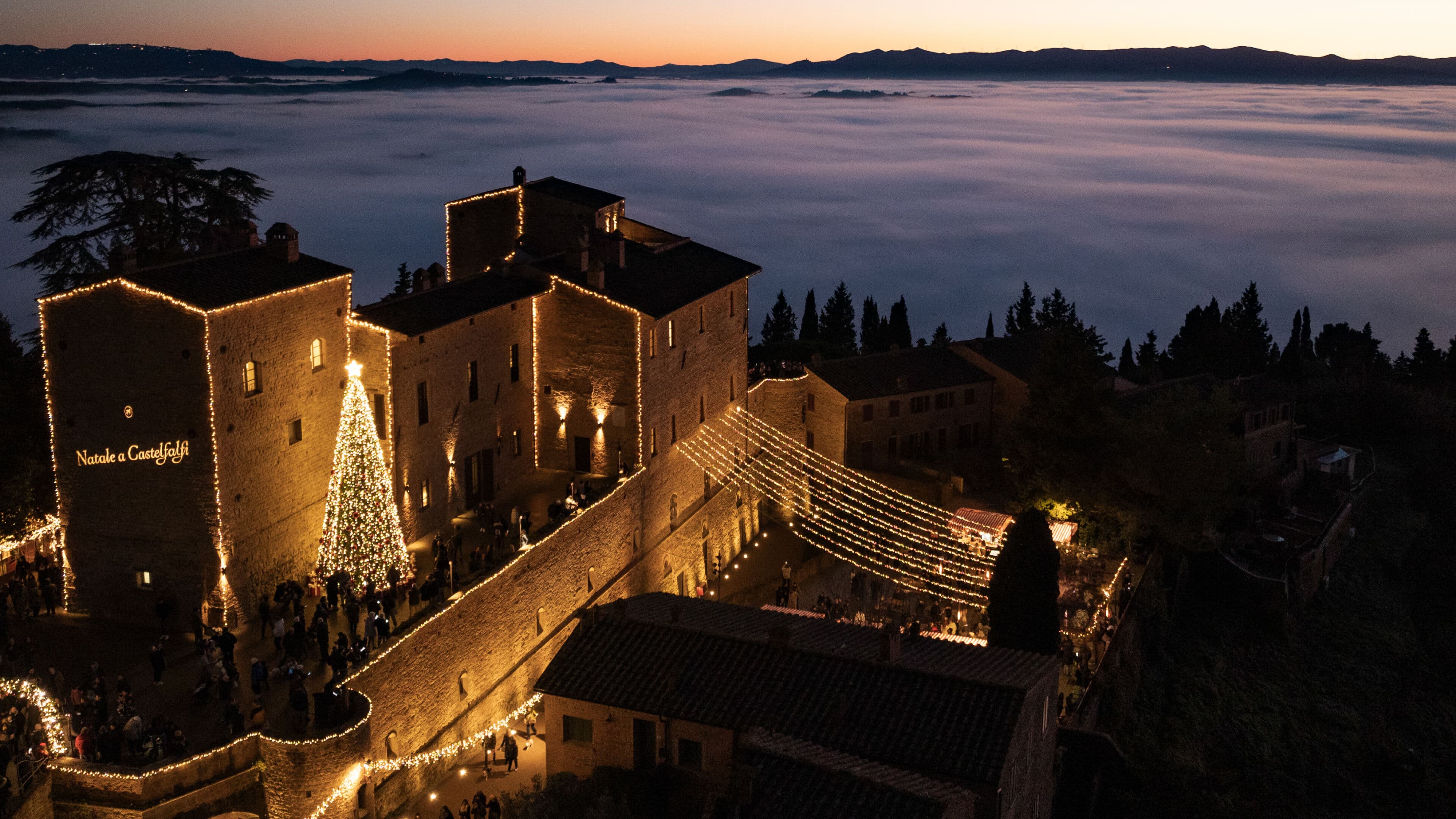 Castelfalfi lit for Christmas above a sea of fog at dusk